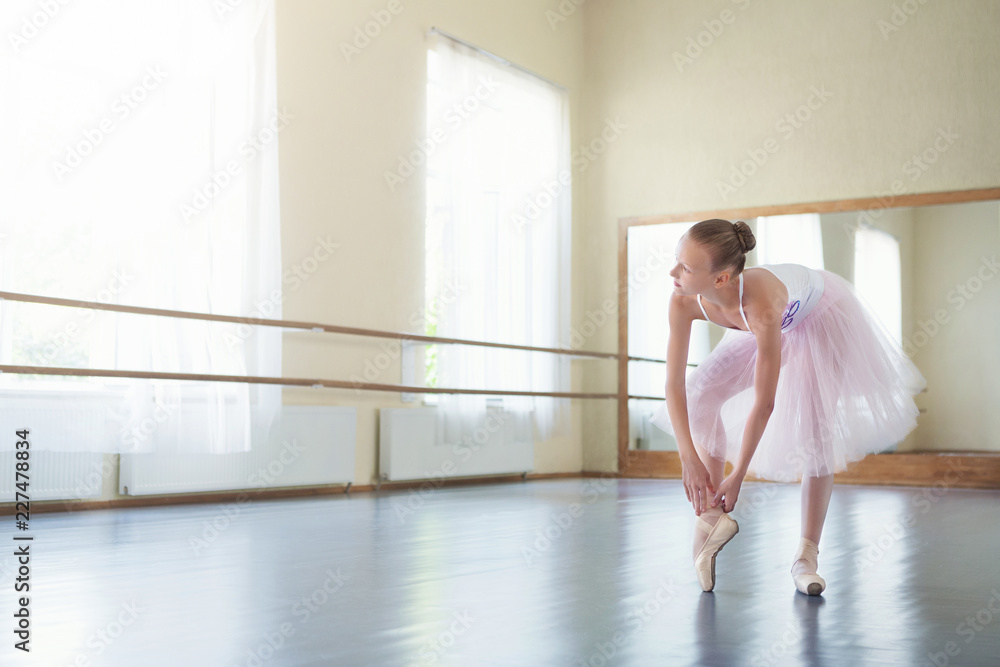 Ballet dancer tying pointe shoes in light studio Ballet dancer tying pointe shoes in light studio