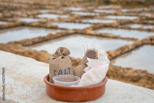 Salinas. Salt Pans or salters at the background with salt bags ready for sale in a basket or bowl outdoor. Hand harvest salt in Gozo Island Marsalforn. space for text.