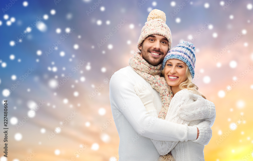 winter, christmas and people concept - smiling couple in hats and knitwear hugging over snow background winter, christmas and people concept - smiling couple in hats and knitwear hugging over snow background