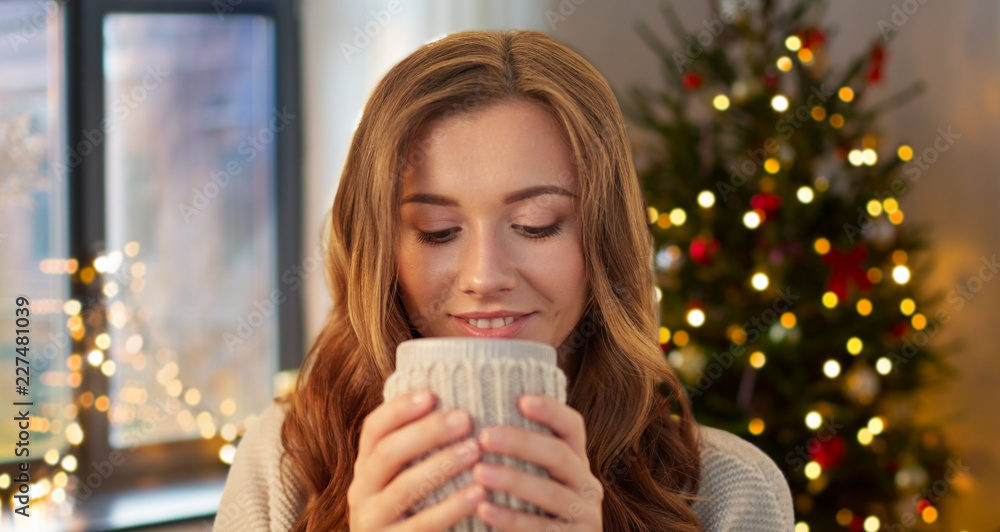 holidays and people concept - happy young woman with cup of coffee or tea at home over christmas tree lights background holidays and people concept - happy young woman with cup of coffee or tea at home over christmas tree lights background