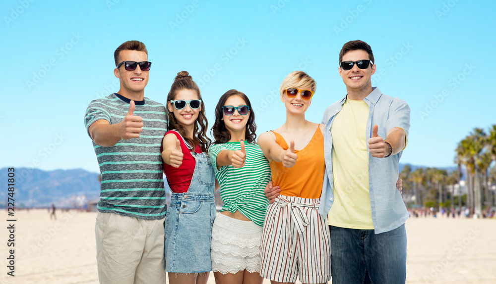 leisure and summer holidays concept - group of happy smiling friends in sunglasses showing thumbs up over venice beach background in california