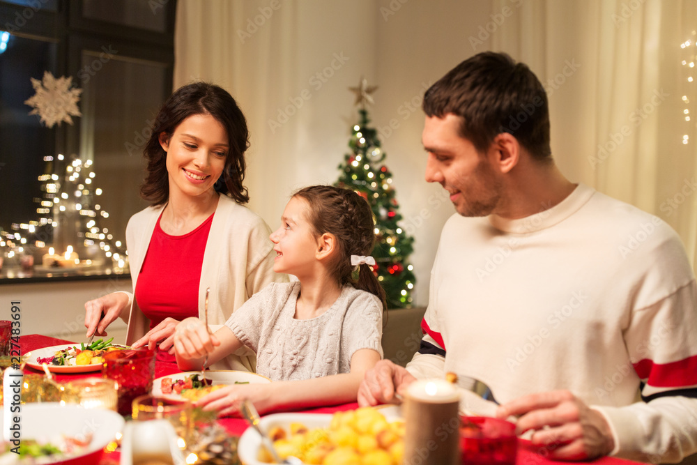 holidays, family and celebration concept - happy mother, father and little daughter having christmas dinner at home