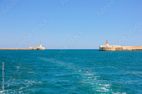 Yacht track on blue water with background of two lighthouses in bright sunny day © Indegerd