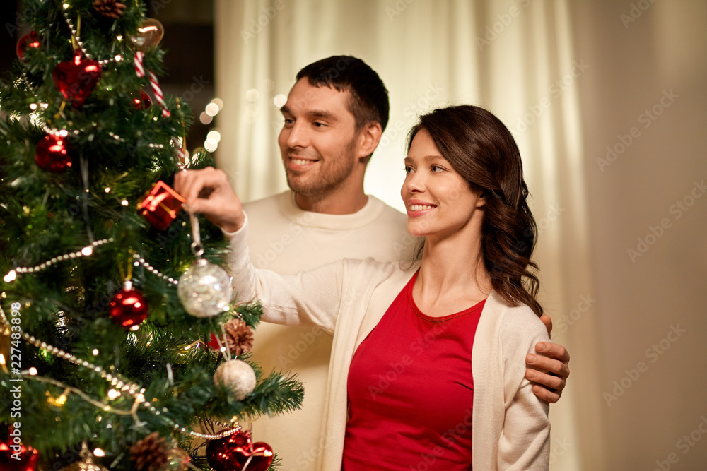 winter holidays and people concept - happy couple decorating christmas tree at home