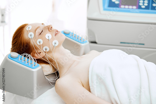 Hardware cosmetology. Face and Body care. Spa treatment. Woman getting electrical musculs stimulation, lying with electrodes on face in beauty salon. photo