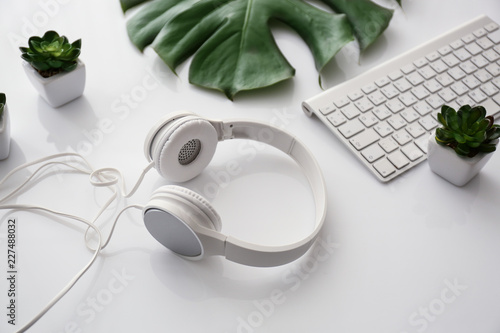 Headphones with computer keyboard and tropical leaf on white table