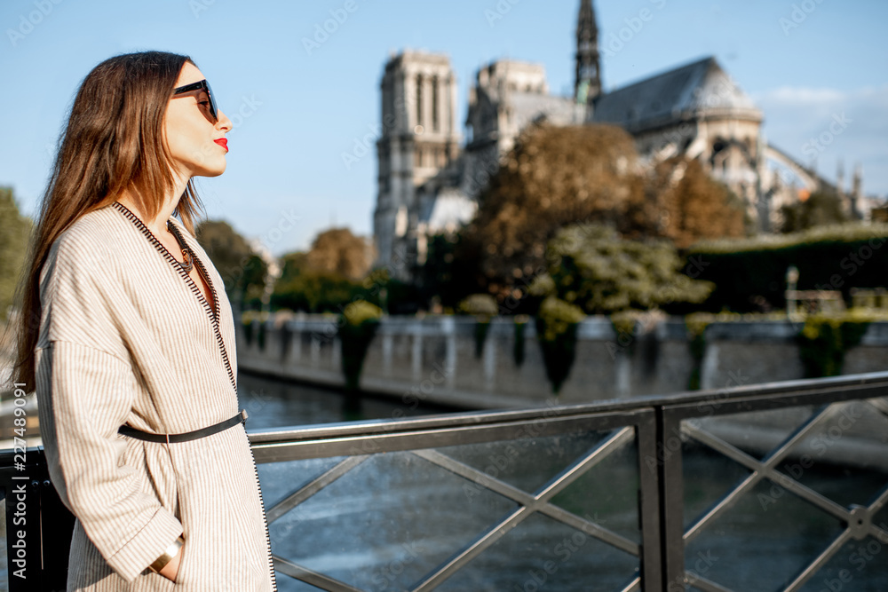 Lifestyle portrait of a young woman walking on the bridge with famous cathedral on the background in Paris, France