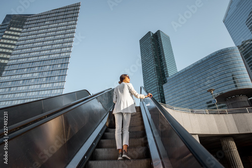 Stylish businesswoman in white suit going up on the escalator at the business centre outdoors with skyscrapers on the background in Paris photo