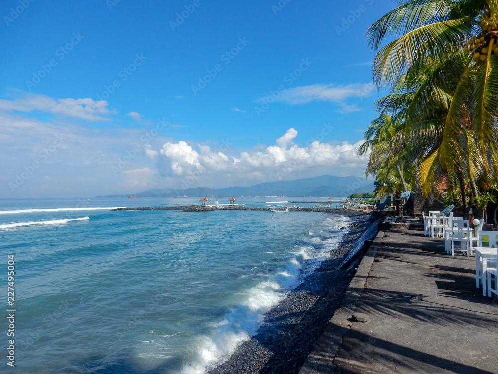 Balinese beach with black sand, palm trees and beach cafe tables