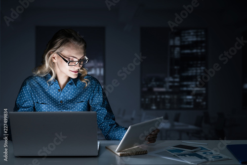 Obraz na płótnie Attractive blonde working on laptop in dark office. Mixed media w salonie