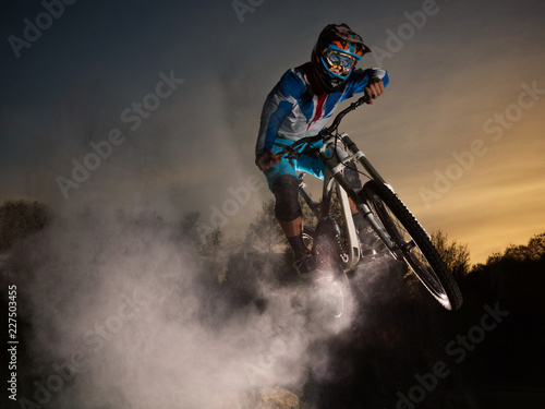 Fototapeta Naklejka Na Ścianę i Meble -  Downhill cycling. Man jump on a mountain bike with dust. Extreme sport.