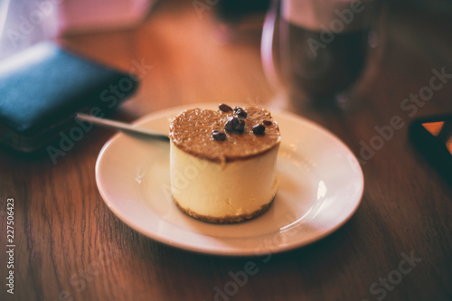 A very yummy vanilla cheesecake next to a wallet and coffee on a wooden table taken at a cafe in Yorkshire, UK