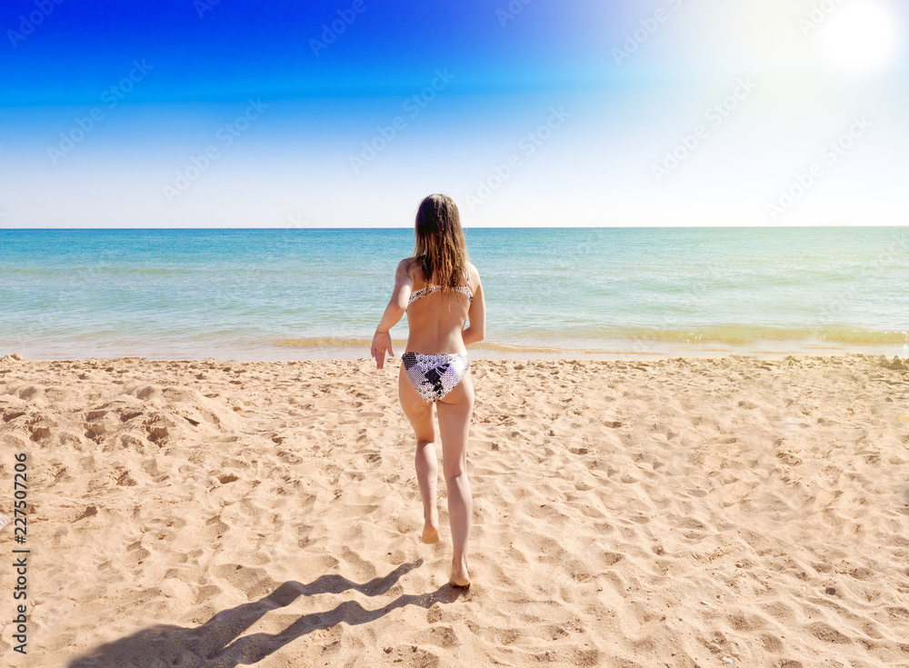 Charming girl in swimwear running on the beach. Back view. Charming girl in swimwear running on the beach. Back view.