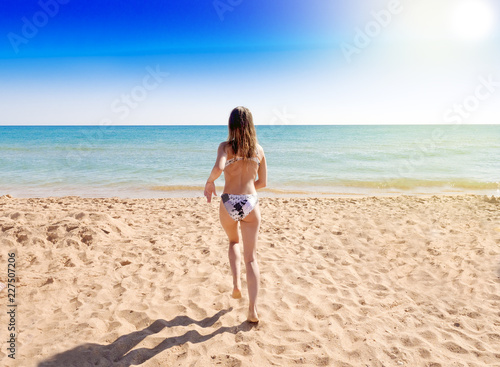 Charming girl in swimwear running on the beach. Back view.