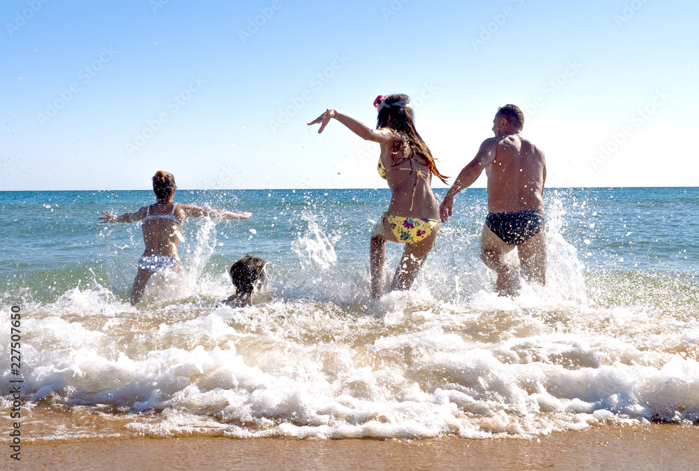 happy young family have fun and live healthy lifestyle on beach.friendship, sea, summer vacation, holidays and people concept - group of smiling friends in swimwear running on beach from back