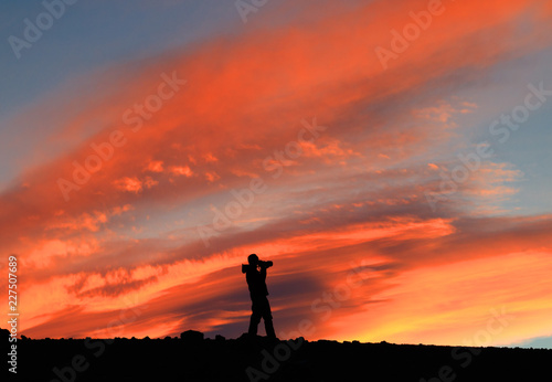 Bright sunset. Photographer with photo camera opposite of the red sky