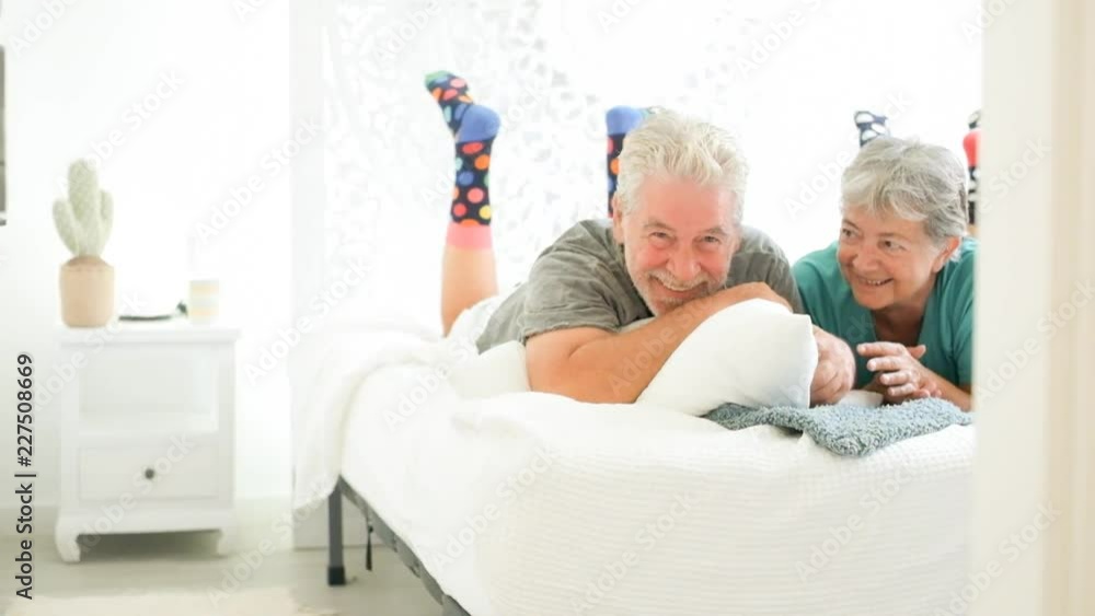 Nice happy cheerful couple of adult senior man and woman playful on the bed at home in bedroom. Lay down and enjoy and smile together for a new happy day morning Nice happy cheerful couple of adult senior man and woman playful on the bed at home in bedroom. Lay down and enjoy and smile together for a new happy day morning