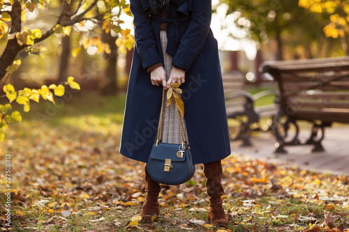 Beautiful fashionable woman walks through the autumn park in a blue coat with a bag in her hands. Details