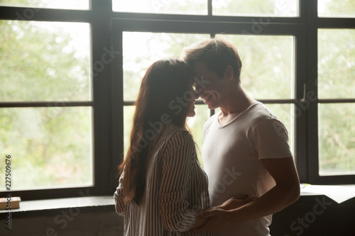 Фотография Young happy guy and girl embracing or dancing together enjoying the company of each other against of window at home, romantic mood