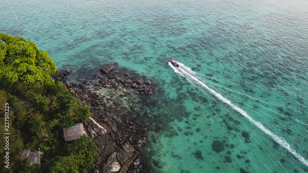 Fototapeta premium Long tail boat passing shores of Phi Phi Island aerial view