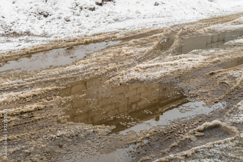 Winter puddles and snow slush on road with traces of tires during the thaw