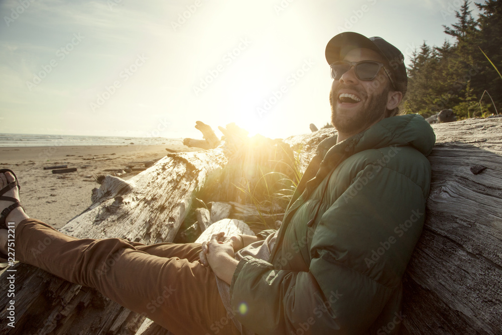 Fototapeta premium Man sitting on log at beach in sunlight