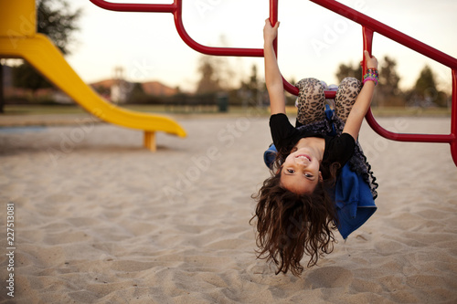 Schilderij op canvas Portrait of girl hanging upside down on monkey bars at park