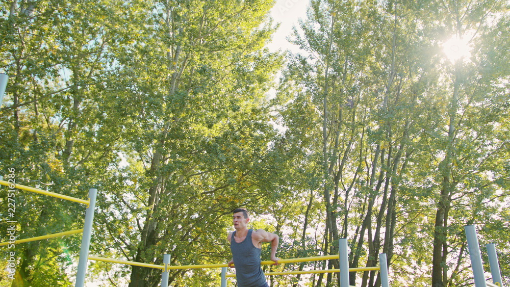 Handsome muscular man doing exercises on horizontal bar outdoors. Calisthenics workout. Slim athlete a very fit guy fitness instructor or a personal trainer working out his arm muscles on outdoor Handsome muscular man doing exercises on horizontal bar outdoors. Calisthenics workout. Slim athlete a very fit guy fitness instructor or a personal trainer working out his arm muscles on outdoor