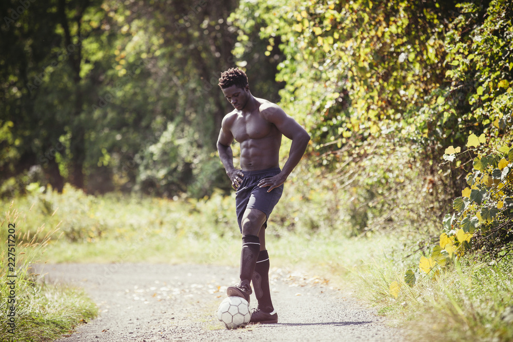 Fototapeta premium Shirtless young man playing with soccer ball on dirt road during sunny day