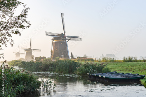 Five rowing boats in the ditch at the three wind mills of Molendriegang Leidschendam, Netherlands during a misty Sunrise