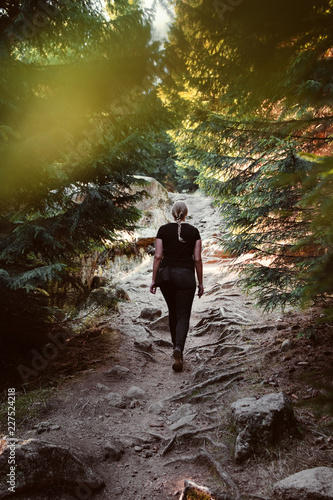 Back view of a blonde girl hiking in a dark moody mountain path in a mysterious nature pine forest. Brocken, nature reserve Harz mountains, National Park Harz in Saxony-Anhalt, Germany