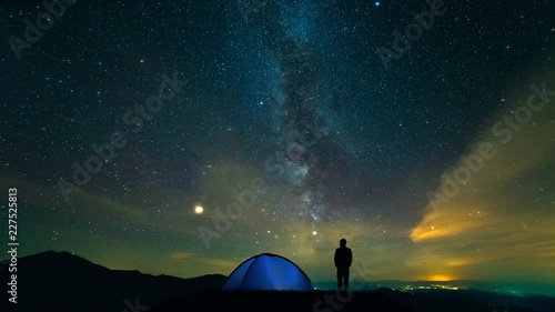 The man near camping tent standing on a meteor shower background. time lapse photo