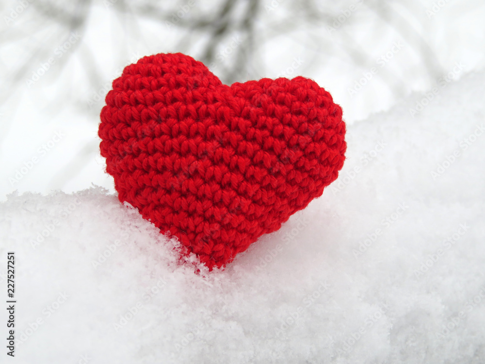 Red knitted heart in the snow, winter weather. Concept for pure love, blood donation, romantic Valentine card