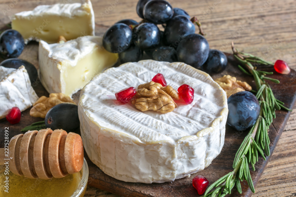 camembert cheese with grapes, pomegranate seeds, honey walnuts and rosemary on wooden cutting board. camembert cheese with grapes, pomegranate seeds, honey walnuts and rosemary on wooden cutting board.