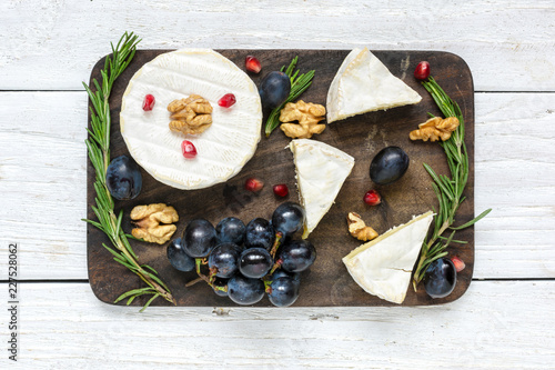 camembert cheese with grapes, pomegranate seeds, walnuts and rosemary on wooden cutting board