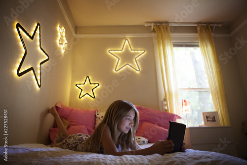 Принти на полотні Smiling girl using tablet computer while lying on bed at home
