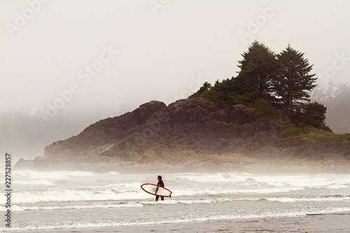 Photography Distant view of man carrying surfboard while walking in sea
