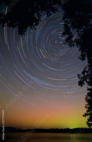 Long exposure star trails, rotating around the North Star. Aurora Borealis glowing green and red above horizon.