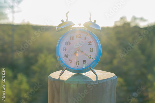 Vintage blue alarm clock on summer forest background. Daylight saving time concept winter time