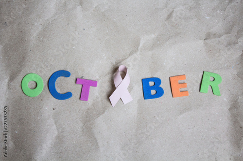 Word October with Pink ribbon symbolic bow color for Breast cancer awareness on craft paper