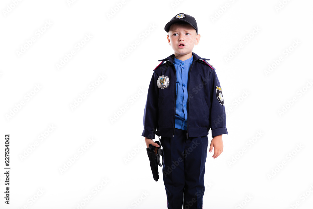 Cute sad little police boy with smile on face and gun on white background. Intelligent cool children in police suit with blue eyes and weapon Cute sad little police boy with smile on face and gun on white background. Intelligent cool children in police suit with blue eyes and weapon