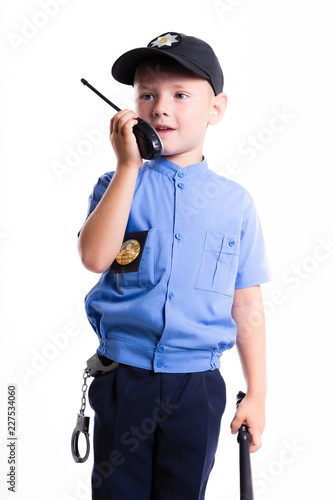 Cute little police boy with smile on face and baton on white background. Intelligent cool children in police suit with blue eyes and baton use radio walkie talkie