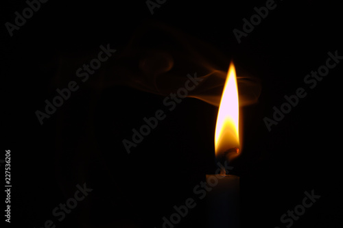 Glowing Orange and White Candle Flame With Swirling Wisps of Smoke Against a Black Background