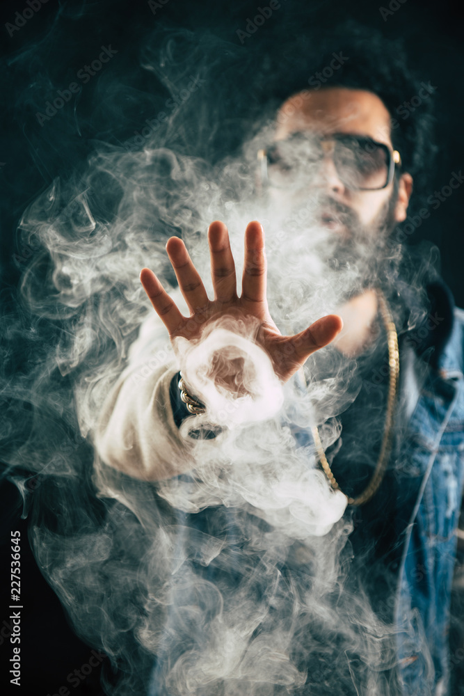 Fototapeta premium Smoking vape. vaping man holding a mod. Vape Rings. A man launches a ring of smoke. Tricks with smoke.