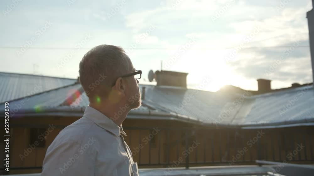 Portrait of pleasant-looking elderly Caucasian man in shirt looking away. Man about fifty years old with grey hair. Roof. Outdoors. Evening. Portrait of pleasant-looking elderly Caucasian man in shirt looking away. Man about fifty years old with grey hair. Roof. Outdoors. Evening.