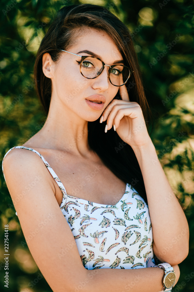 Fototapeta premium Closeup emotional lifestyle portrait of adorable beautiful young cheerful coquette fashionable girl in trendy glasses with big natural lips and blue happy eyes smiling outdoor at nature in summer.