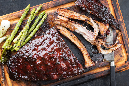 Barbecue spare ribs St Louis cut with hot honey chili marinade and green asparagus as top view on an old rustic board