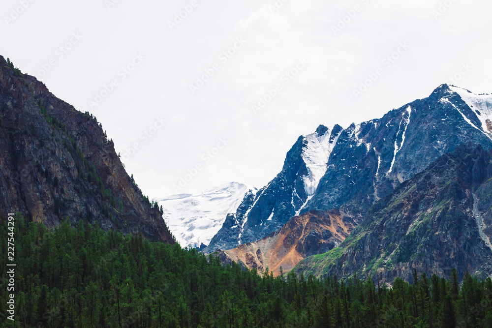 Giant snowy mountain top under cloudy sky close up. Rocky ridge in overcast weather. Copy space on white snow of glacier. Atmospheric landscape of majestic nature.