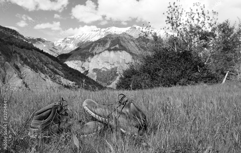 Old hiking shoes and Alpine landscape at background. Provence-Alpes-Cote d'Azur region of France. Black and white photo. 