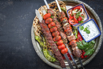 Traditional oriental Adana kebap and shashlik skewer with tomato and flatbread as top view on a plate with copy space left